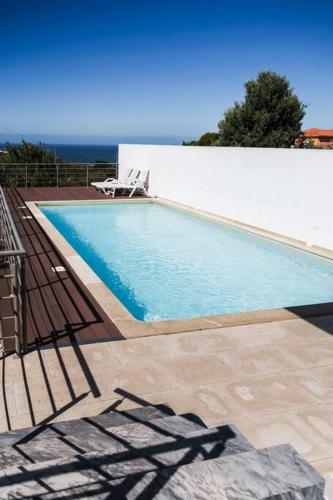 a swimming pool with two lawn chairs and the ocean at Casa Amour Villa in Lourinhã