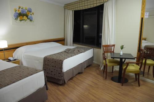a hotel room with two beds and a table and a window at Hotel Golden Park Internacional Foz & Convenções By Nacional Inn in Foz do Iguaçu