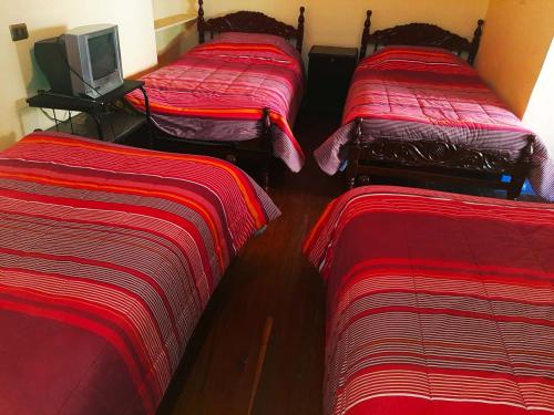 trzy łóżka w pokoju z czerwoną pościelą i telewizorem w obiekcie Hostal Compañía de Jesús w mieście Potosí