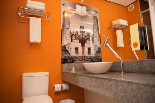 a bathroom with a sink and a toilet with an orange wall at Partner Caxias do Sul in Caxias do Sul