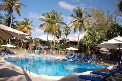 una piscina con sillas, sombrillas y palmeras en Res MARINA-CARAYOU 1, en Les Trois-Îlets