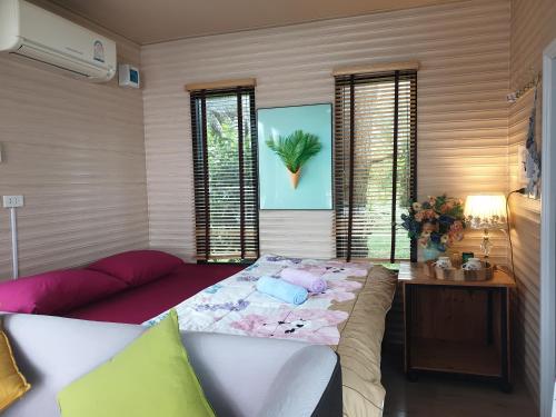a bedroom with a bed and a table and windows at บ้านสวนริมน้ำเขาค้อ in Khao Kho