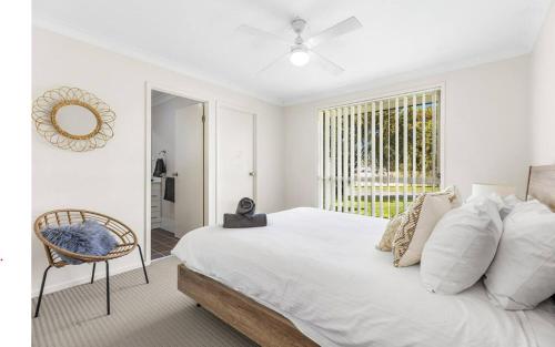 a white bedroom with a bed and a chair at Hunter Home with POOL / CINEMA ROOM / PING PONG in Cessnock