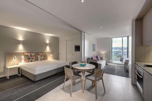 Adina Apartment Hotel Bondi Beach Sydney في سيدني: غرفة فندقية بسرير وطاولة وكراسي