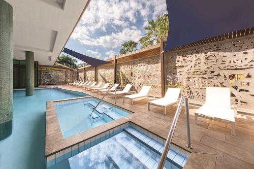 an indoor swimming pool with white chairs and a building at Vibe Hotel Darwin Waterfront in Darwin
