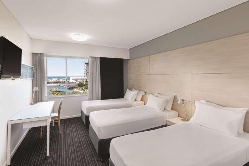 a hotel room with two beds and a desk at Vibe Hotel Darwin Waterfront in Darwin