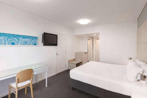 a room with a bed and a desk and a tv at Vibe Hotel Darwin Waterfront in Darwin