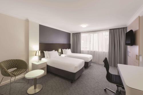 パースにあるランデブー ホテル パース セントラルのベッド2台とデスクが備わるホテルルームです。