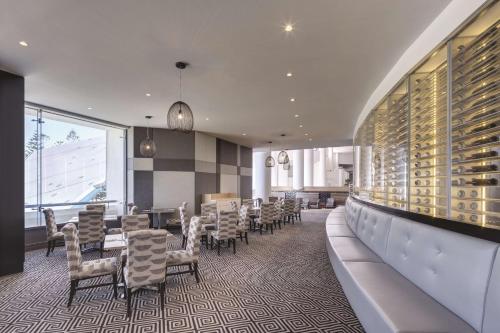 a dining room with tables and chairs and a wall of wine bottles at Rendezvous Hotel Perth Scarborough in Perth