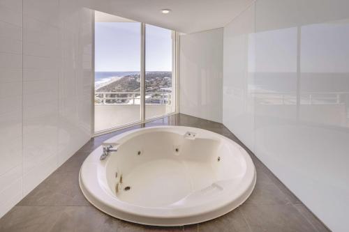 a large white bath tub in a room with windows at Rendezvous Hotel Perth Scarborough in Perth