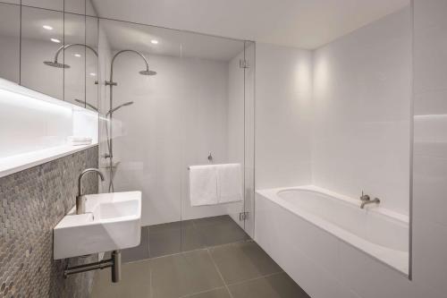 a white bathroom with a sink and a bath tub at Vibe Hotel Canberra in Canberra