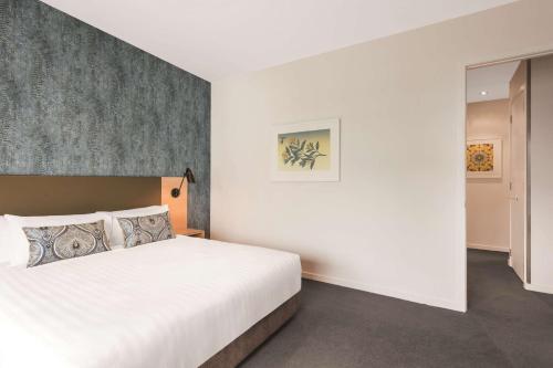 a bedroom with a white bed and a wall at Adina Apartment Hotel Auckland Britomart in Auckland