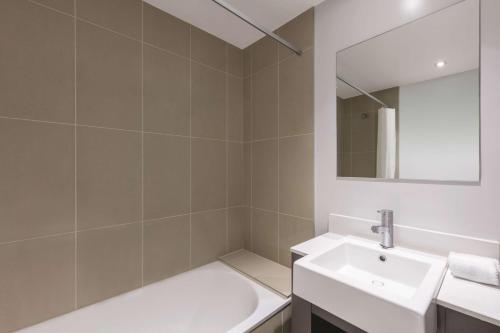 a white bathroom with a sink and a mirror at Adina Apartment Hotel Auckland Britomart in Auckland