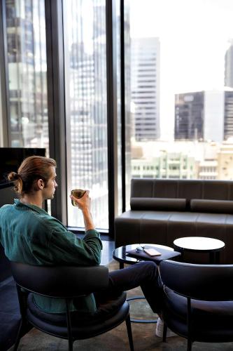 a woman sitting in a chair eating food in front of a window at A by Adina Sydney in Sydney