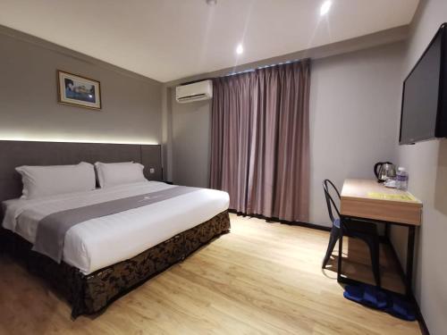 een slaapkamer met een bed, een bureau en een televisie bij OCEAN HOTEL in Labuan