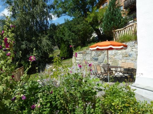 un jardín con mesa, sombrilla y flores en Ferienhaus Turilji en Albinen