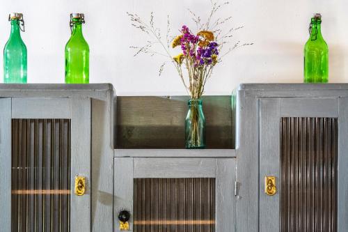 two green bottles and a vase with flowers on a cabinet at Ferrata Vár Vendégház in Csesznek