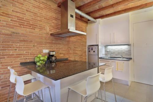 a kitchen with a counter with white chairs and a brick wall at AG Apartments in Barcelona