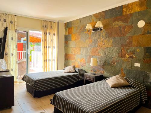 a bedroom with two beds and a stone wall at Hotel La Aldea Suites in La Aldea de San Nicolas