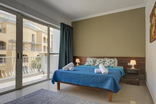 - une chambre avec un lit bleu et une grande fenêtre dans l'établissement Violet Court Apartments and Penthouse in St Julian's By ShortletsMalta, à San Ġiljan