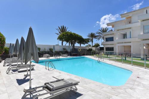 uma piscina com cadeiras e guarda-sóis ao lado de um edifício em Apartment Aida 202 by VillaGranCanaria em Playa del Inglés
