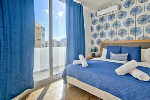 een slaapkamer met een blauw bed met blauwe gordijnen en een raam bij Tower Road - Central Sliema Modern Apartments and Duplex Penthouse by ShortletsMalta in Sliema