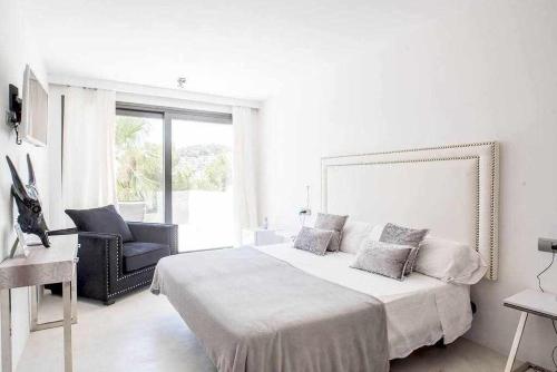 a white bedroom with a large bed and a chair at Balinese Villa near the beach outdoor jacuzzi in Cala Llonga