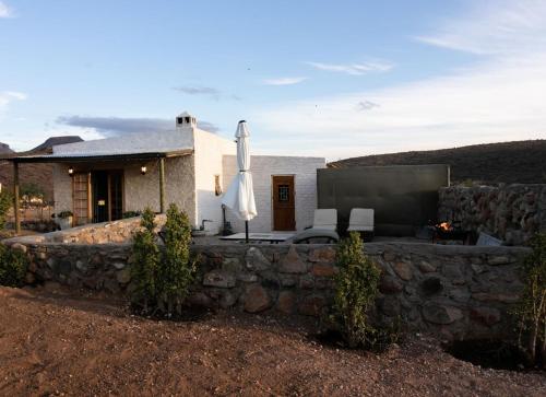 a house with a stone wall and an umbrella at Wild Olive Cottage in Graaff-Reinet