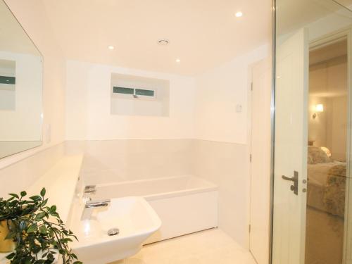 a white bathroom with a sink and a bath tub at Mill Cottage in Upwey