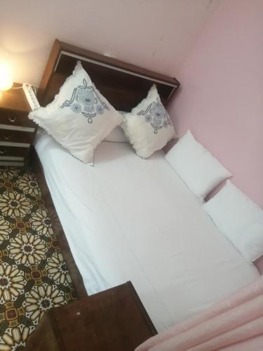 um quarto com uma cama com lençóis brancos e almofadas em Bab aissi home em Meknès