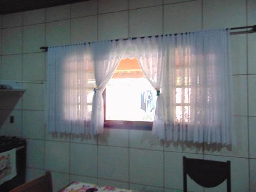 a window with white curtains in a kitchen at Rancho do Colega in Santa Branca