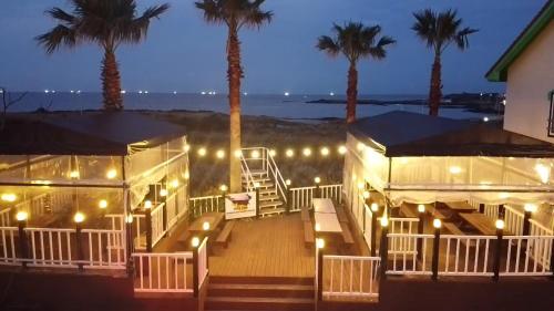 a deck with lights and palm trees at night at Morning Beach Pension in Jeju
