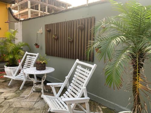 tres sillas blancas y una mesa y una palmera en Lindo Sobrado Amarelo -próximo a praia, en Mongaguá