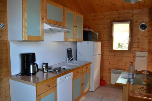 La cuisine est équipée d'un réfrigérateur blanc et d'un évier. dans l'établissement Volcans Vacances Les Chalets Du Lac, à Aydat