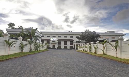 een wit gebouw met een hek en een oprit bij Treebo Tryst Vahada in Alleppey