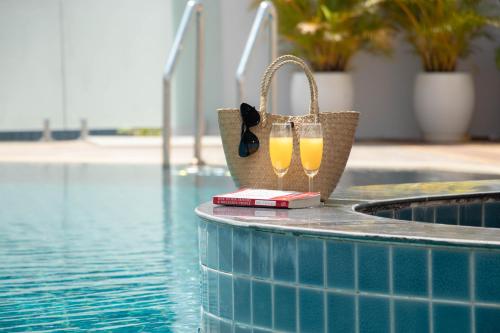 a purse and two glasses of wine next to a swimming pool at Urbanite Hotel in Vientiane