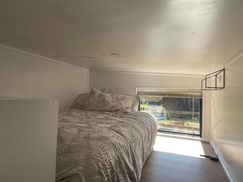 a bed in a small room with a window at Tiny House in the Bush - a minute from town centre in Raetihi