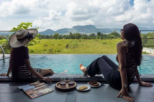 two women sitting next to a swimming pool with food at Two Villa by StayVista with Infinity Pool, Farm & Mountain Views, Modern Interiors in Karjat