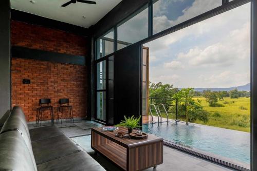 a living room with a couch and a large window at Two Villa by StayVista with Infinity Pool, Farm & Mountain Views, Modern Interiors in Karjat