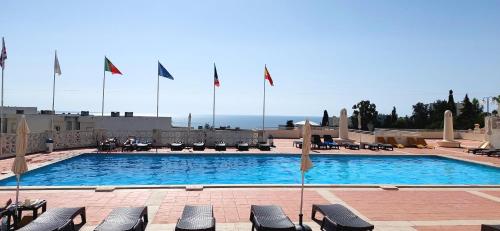a large swimming pool with lounge chairs and flags at Sol Brilhante in Albufeira