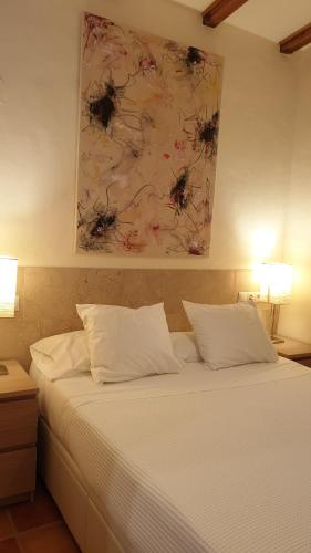 a bed with white sheets and a painting on the wall at Las casas de Colinas in Vejer de la Frontera