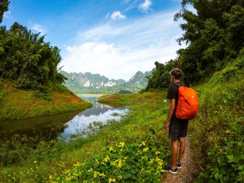 a man with an orange backpack looking at a river at Monkey Mansion - Jungalows & Tours in Khao Sok