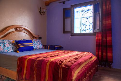 Blue House Town في شفشاون: غرفة نوم مع سرير مع نافذة زجاجية ملطخة