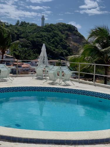 una piscina con sillas, una mesa y una sombrilla en Pousada Farol do Morro, en Morro de São Paulo