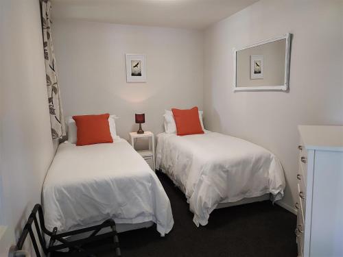 two beds in a room with white and orange pillows at Cornwallis Palms in Auckland