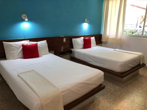 two beds with red pillows in a hotel room at Hotel Los Leones in Palenque