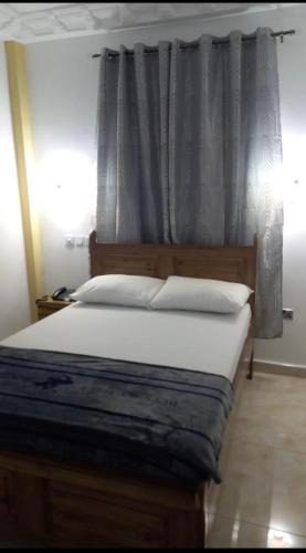 ein Bett in einem Schlafzimmer mit einem Fenster mit einem Vorhang in der Unterkunft BAFFOUR STUDIO in Kumasi