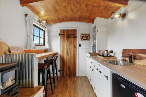 a kitchen with white cabinets and a wooden ceiling at The Shepherds Hut - boutique retreat. in Hanmer Springs