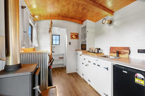 a kitchen with white cabinets and a wooden ceiling at The Shepherds Hut - boutique retreat. in Hanmer Springs