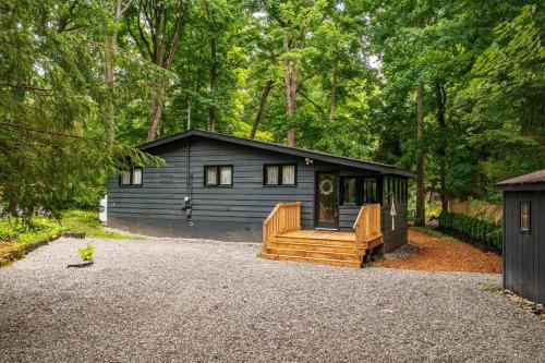 una cabaña negra en el bosque con un porche y una casa en Black River Haus - Scandinavian Riverfront Cabin Muskoka en Washago